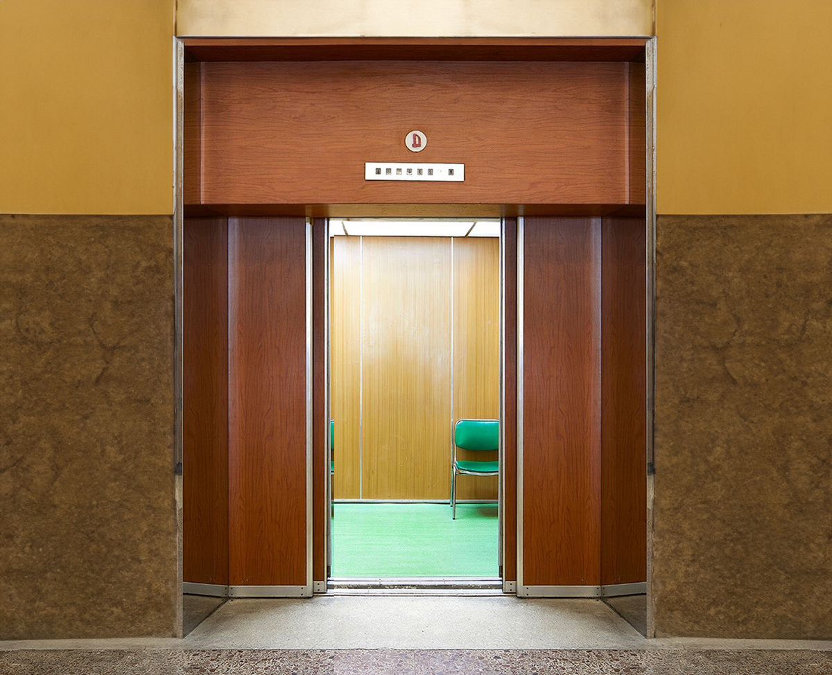Mid-century elevator with wood-panel doors and a green chair inside